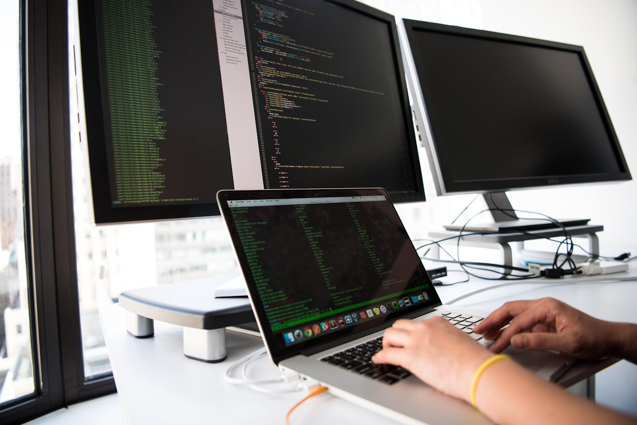 creative-02 A developer writes code on a laptop in front of multiple monitors in an office setting.