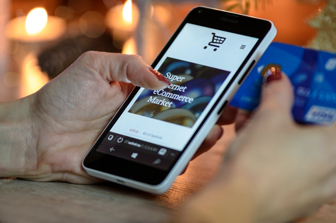creative-03 Woman using smartphone for online shopping with credit card in hand, festive background lighting.